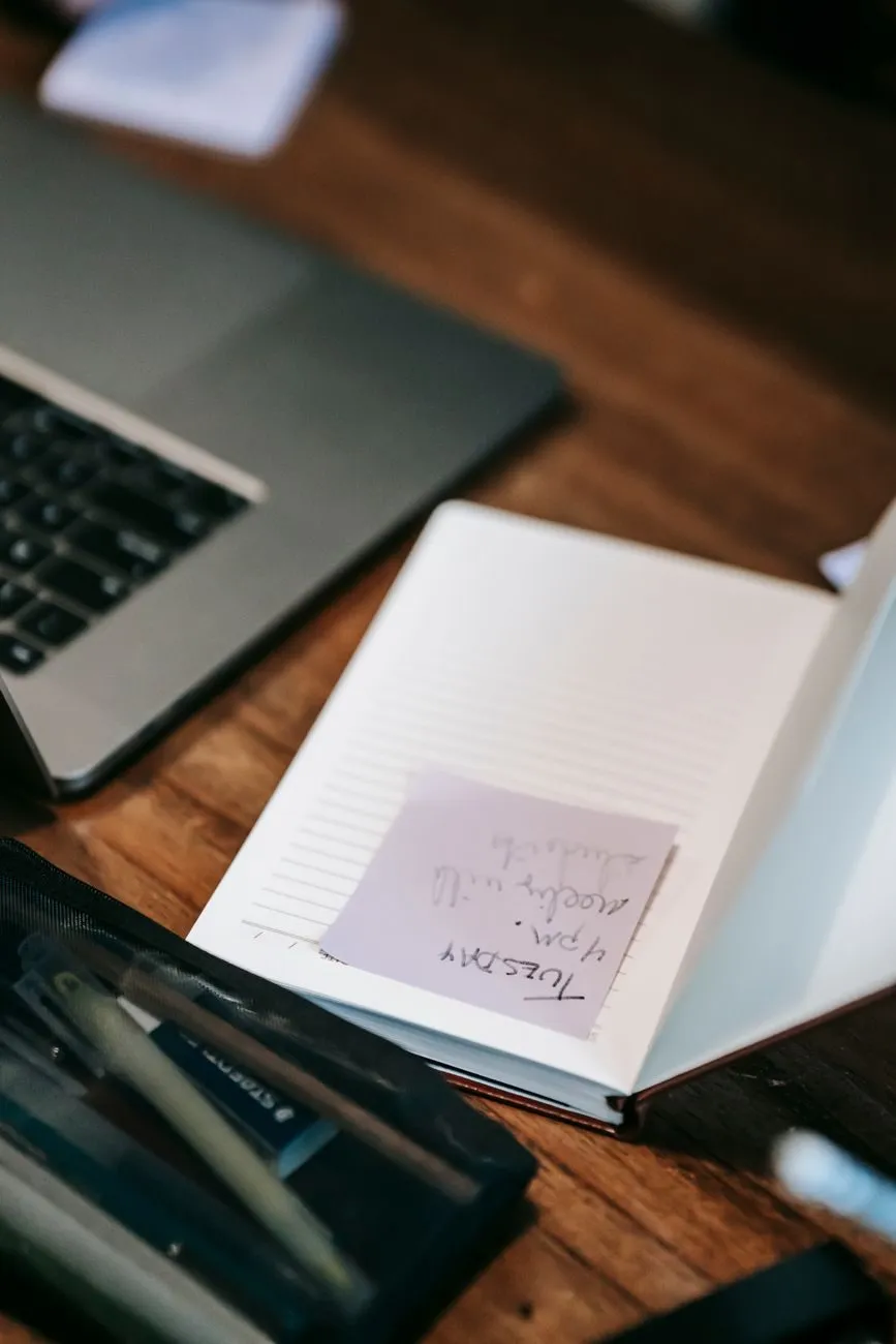 Notesbog og pen på et skrivebord ved en computer